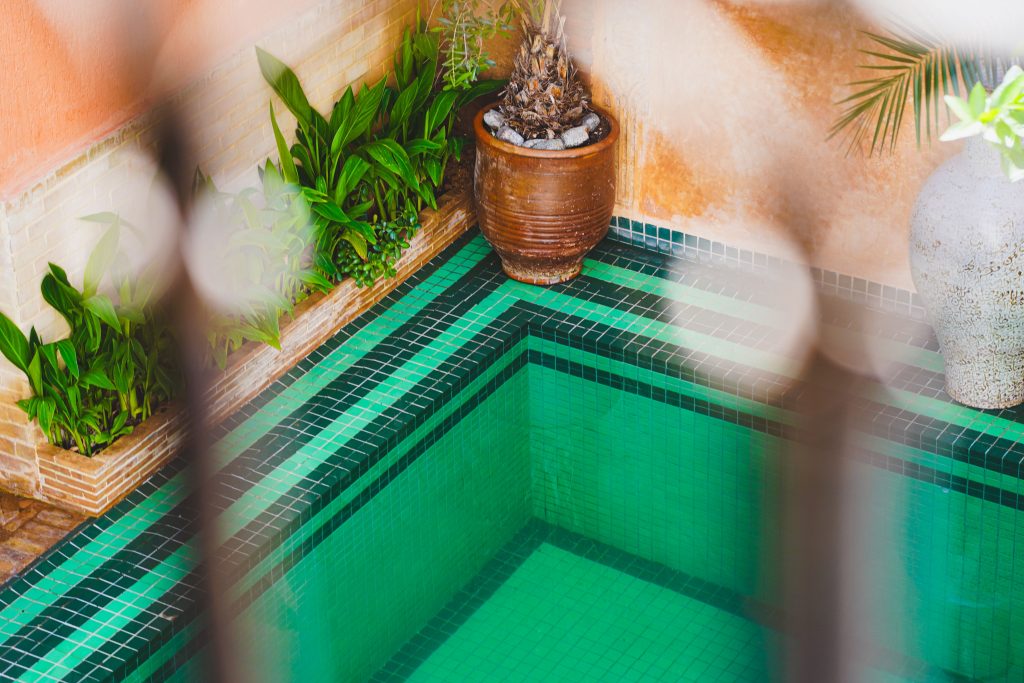 Compact green tiled plunge pool tucked into a courtyard corner surrounded by potted plants