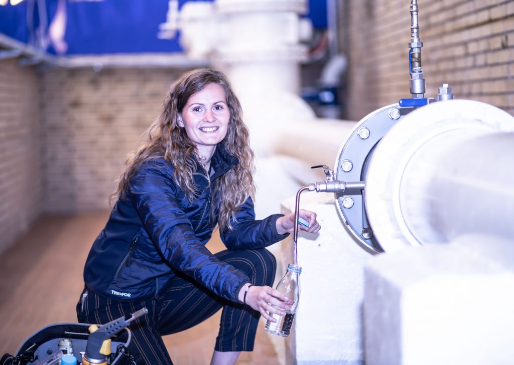 Professional female technician sampling water near a technical equipment installation