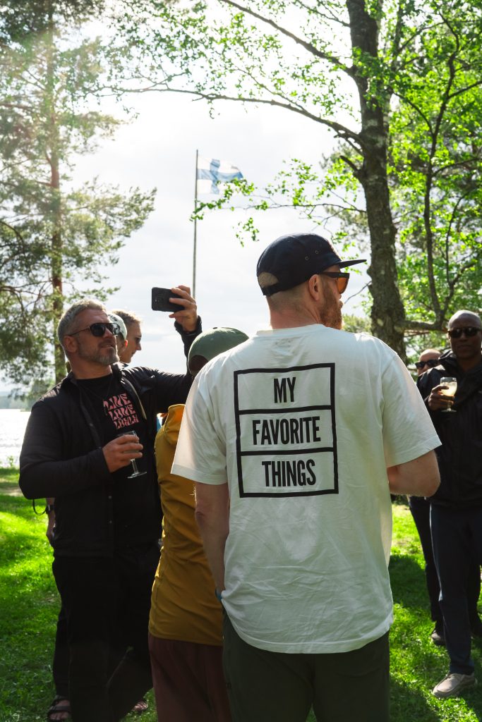 Group of people gathering outdoors with a Finnish flag flying in the background.