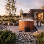 Holl's Olma round Nordic bath installed on a wooden deck in a modern garden at sunset