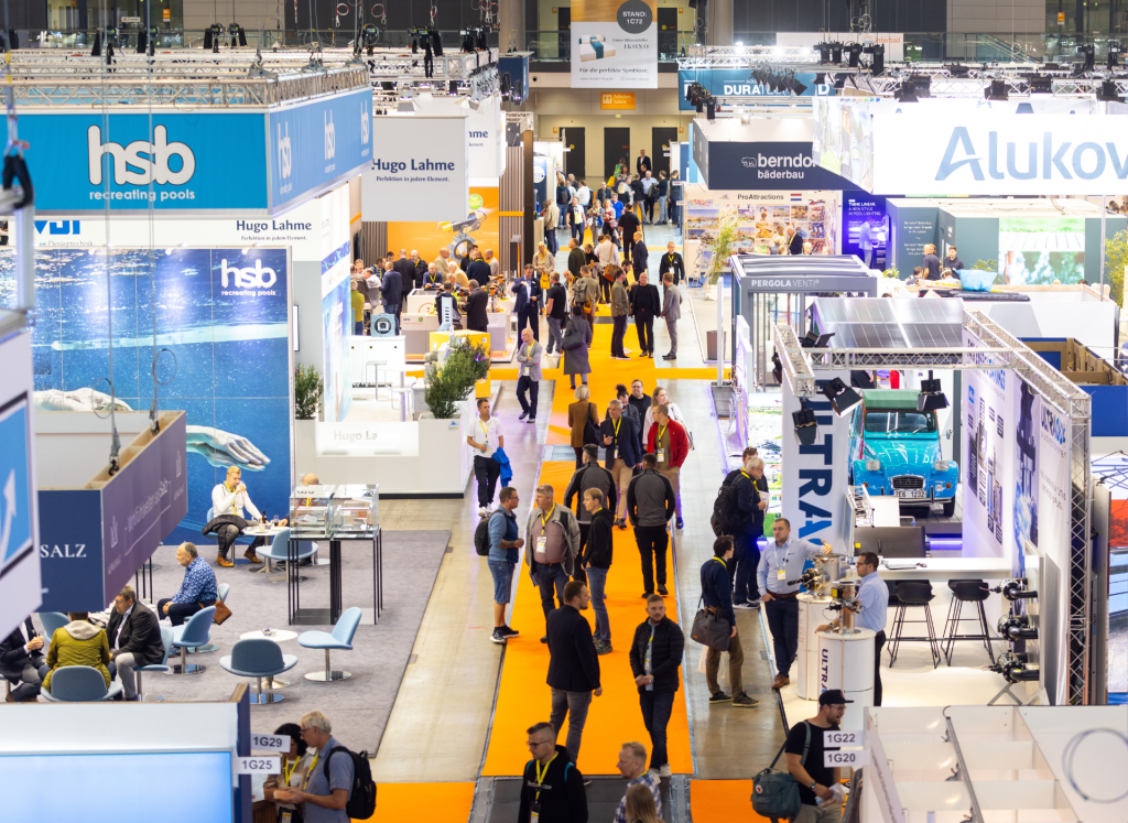 High-angle view of a busy exhibition hall at interbad showing carpeted aisles, trade booths, and visitors walking through the venue.