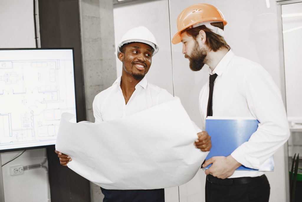 Two construction professionals in hard hats reviewing building blueprints and compliance documents.