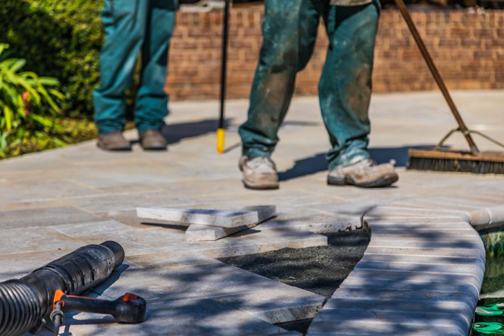 Low-angle shot of pool contractors working on stone paving and tile installation around a swimming pool edge.