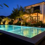 Residential back garden with swimming pool softly lit in green and turquoise light at twilight