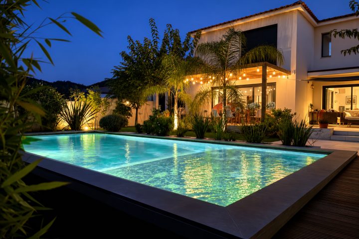 Residential back garden with swimming pool softly lit in green and turquoise light at twilight