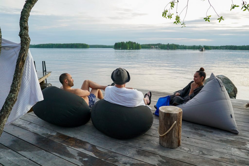 People relaxing on beanbag chairs on a wooden dock overlooking a Finnish lake after a sauna session   