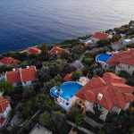 High angle aerial shot of luxury coastal houses featuring private blue swimming pools surrounded by green trees