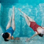 Top view of two women floating and relaxing in a blue mosaic tiled hydrotherapy spa pool