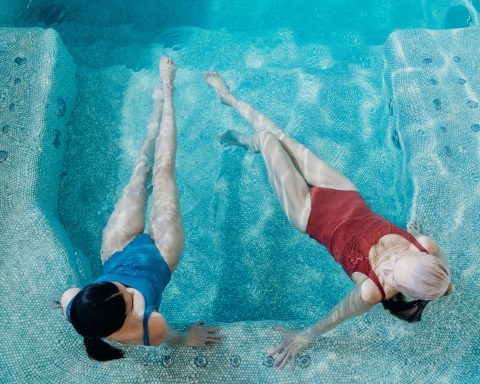 Top view of two women floating and relaxing in a blue mosaic tiled hydrotherapy spa pool