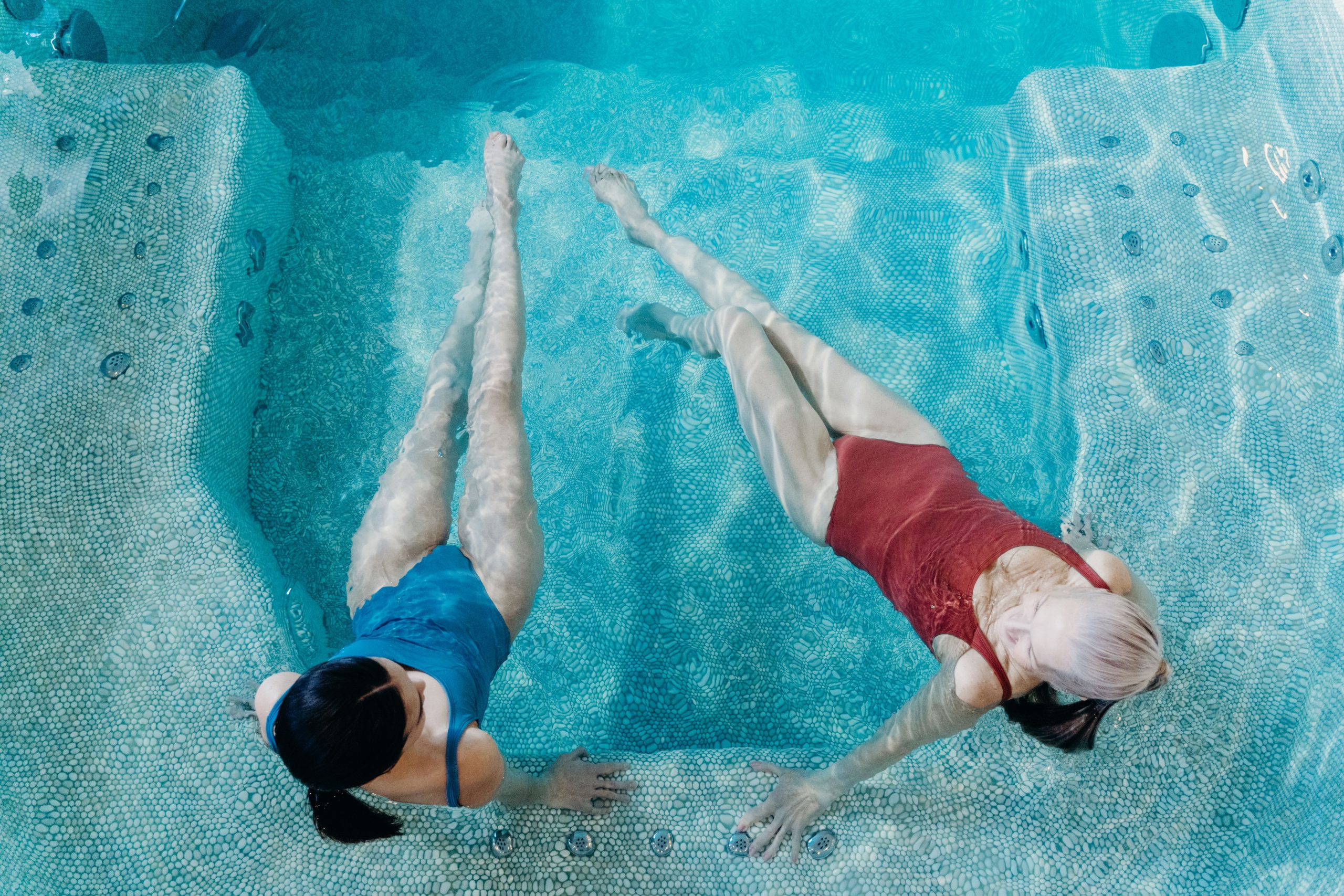 Top view of two women floating and relaxing in a blue mosaic tiled hydrotherapy spa pool